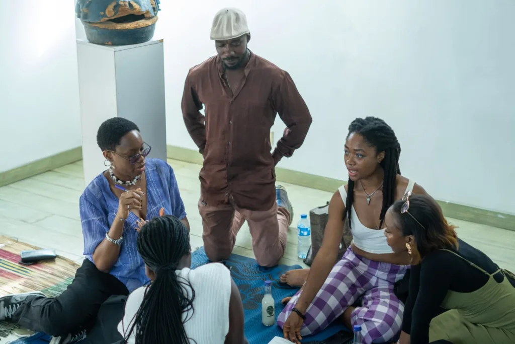 Participants having a discourse. They are 5 in number, all seated on a mat while talking.